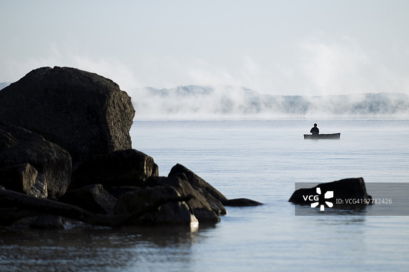 男子在缅因州塞巴戈湖的独木舟上雾中钓鱼图片素材