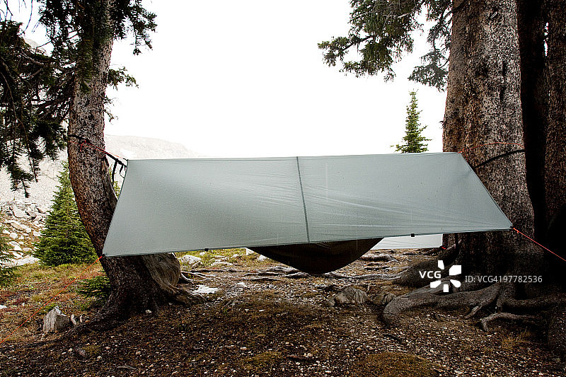 在怀俄明州雪山山脉的雨天，一名男子在带防雨罩的吊床上小憩图片素材