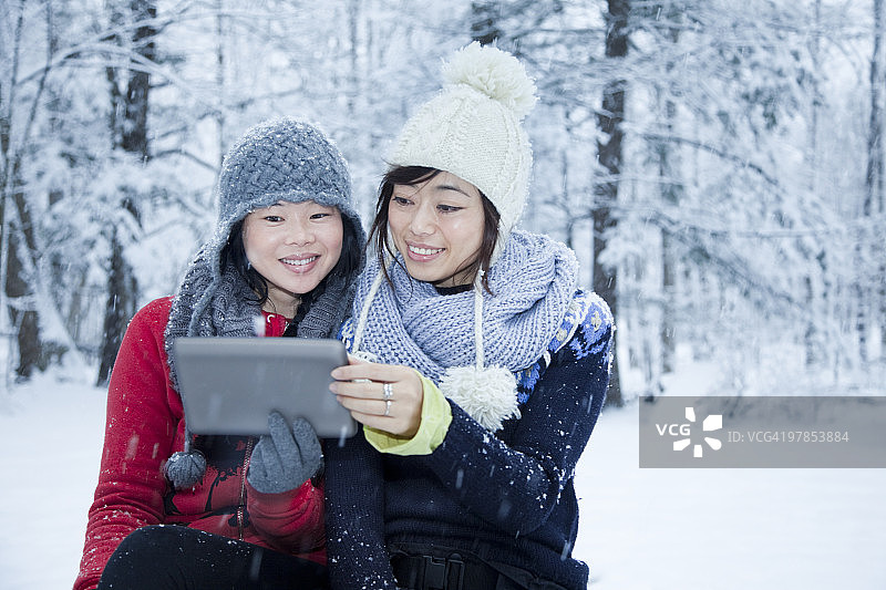 两位女性看着平板电脑，下着雪图片素材