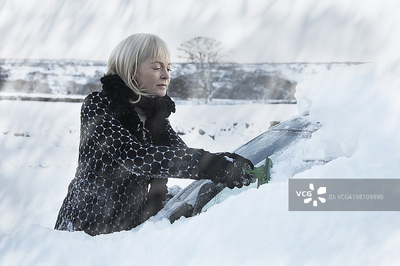 女人刮掉汽车挡风玻璃上的雪图片素材