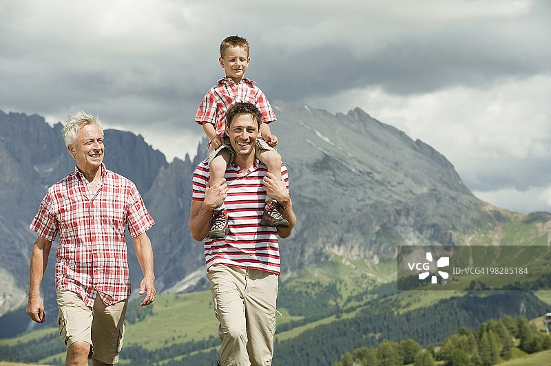 意大利塞iseralm，祖父、父亲和儿子(6-7)在草地上行走，微笑，肖像图片素材
