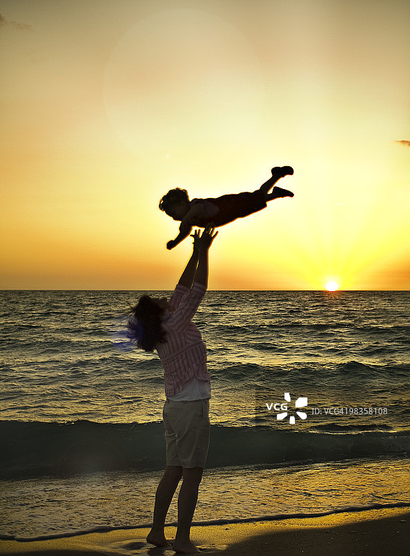 夕阳下妈妈在海滩上抛接幼儿图片素材