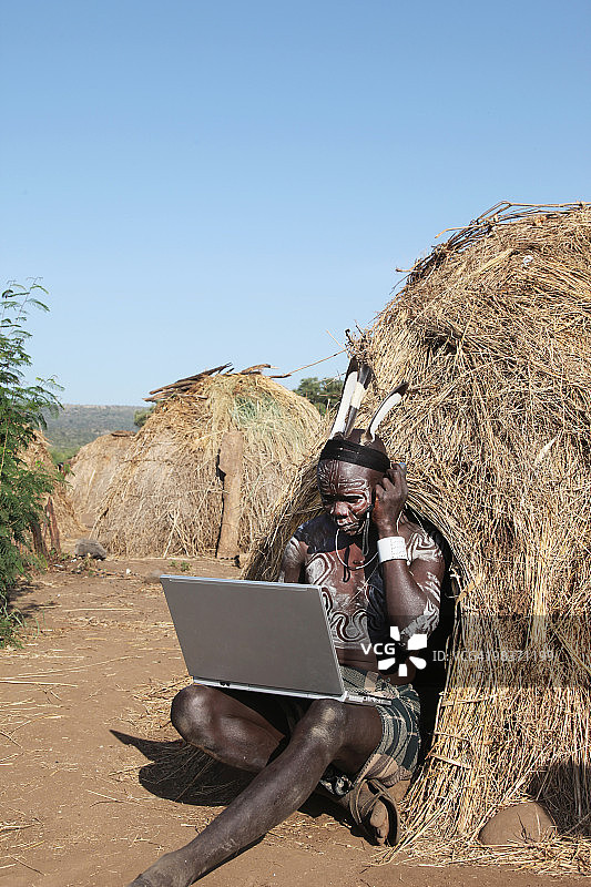 使用手机和笔记本电脑的穆尔西部落男人图片素材