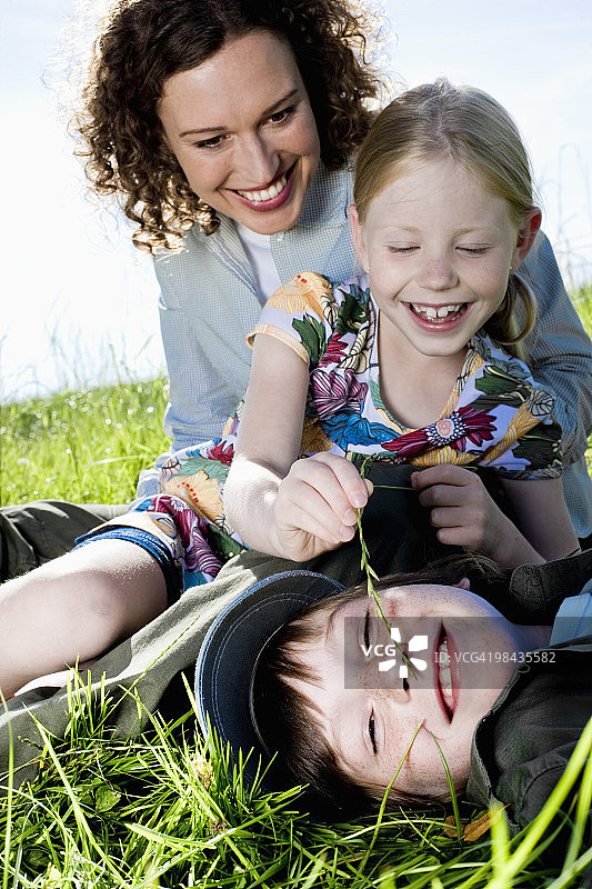 用草叶挠弟弟痒痒的年轻女孩图片素材
