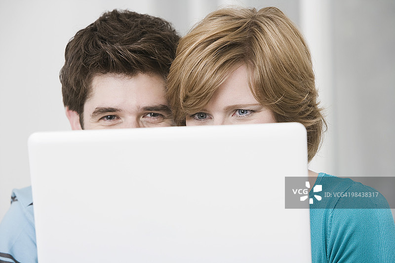 年轻情侣躲在笔记本电脑后面图片素材