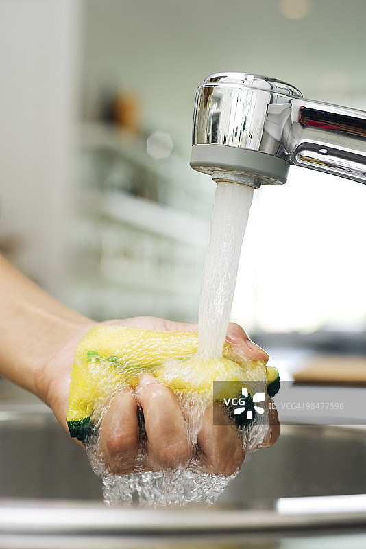在厨房水龙头下冲洗海绵的人图片素材