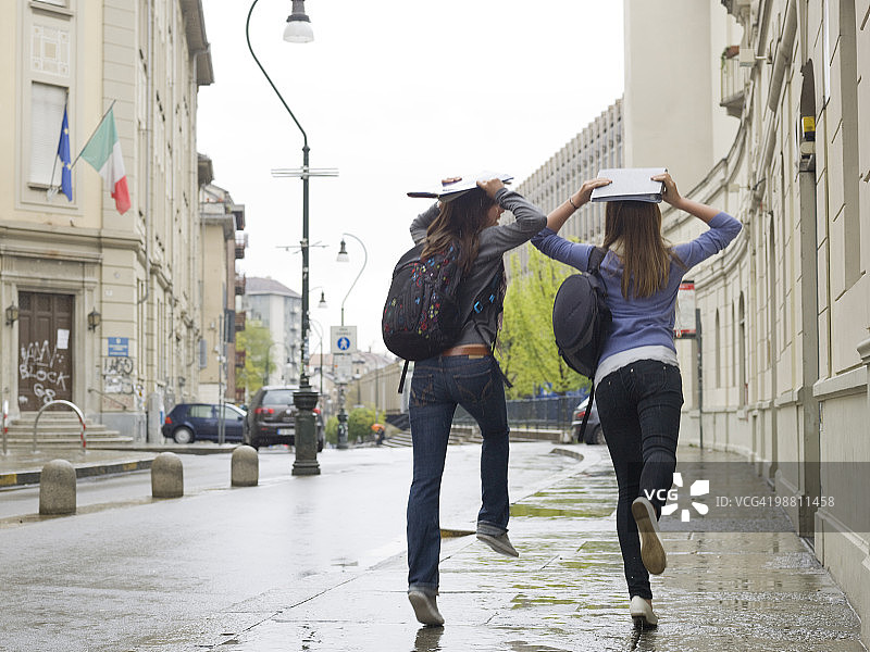少女们在雨中跑到学校，用书本挡雨图片素材