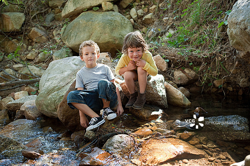 男孩们坐在河边的岩石上图片素材