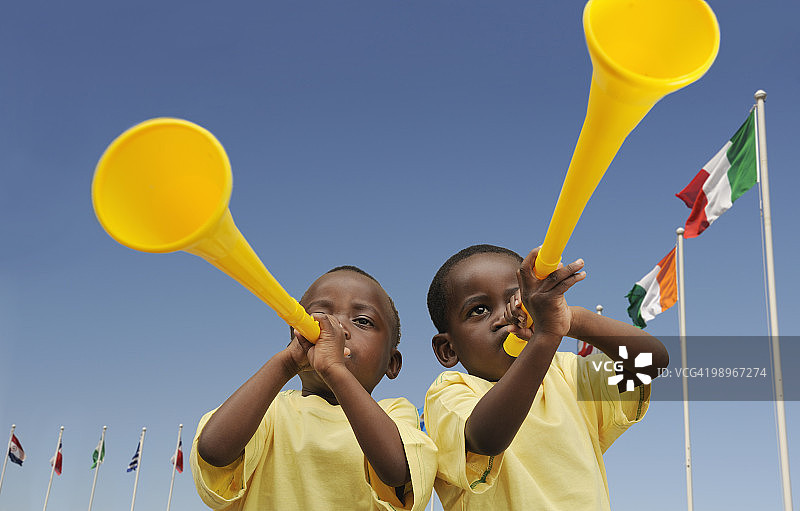 两名（2-3岁）男孩拿着黄色呜呜祖啦，南非西开普省开普敦图片素材