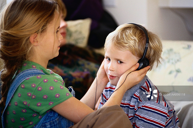女孩帮助幼儿戴耳机听音乐图片素材