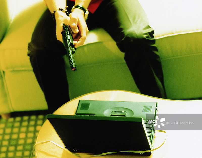 男人用枪指着笔记本电脑图片素材