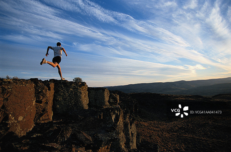 男子在悬崖顶上奔跑，日落时分的背影图片素材