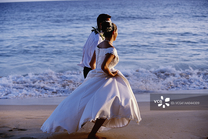在海滩上奔跑的年轻新娘和新郎（侧面视角）图片素材