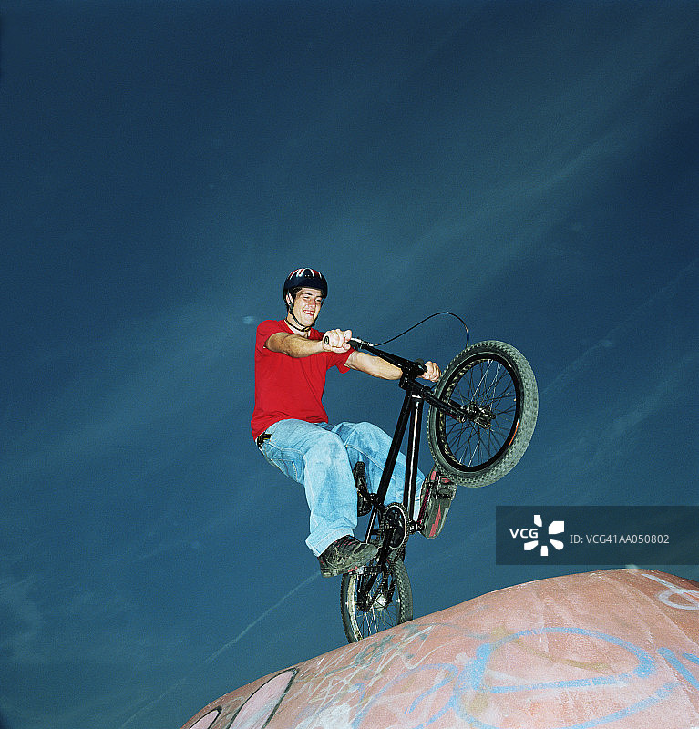 年轻男子表演自行车特技，低角度拍摄图片素材