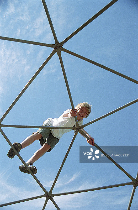 男孩在户外公园的健身器材上攀爬（仰视）图片素材