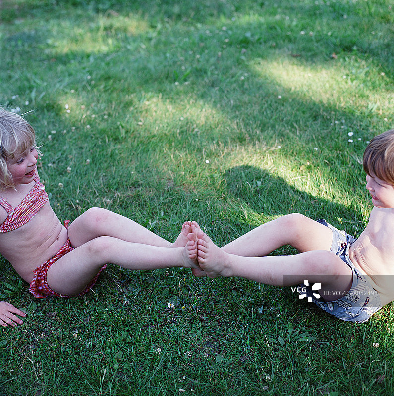 坐在草地上脚碰脚的兄妹（3-5岁）图片素材