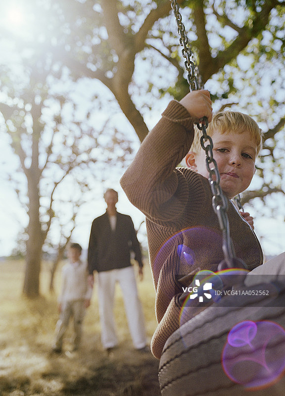 在轮胎秋千上的4-6岁男孩，背景是父亲和兄弟图片素材