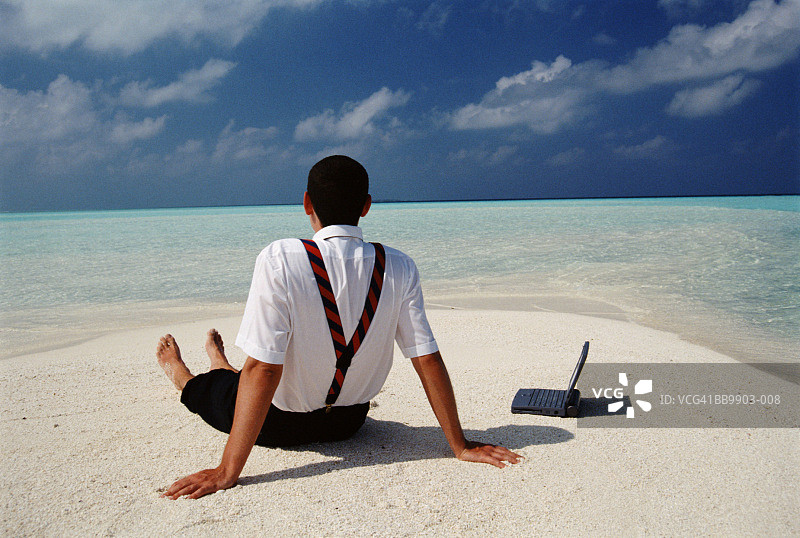 坐在沙滩上，带着笔记本电脑的男高管，后视图图片素材