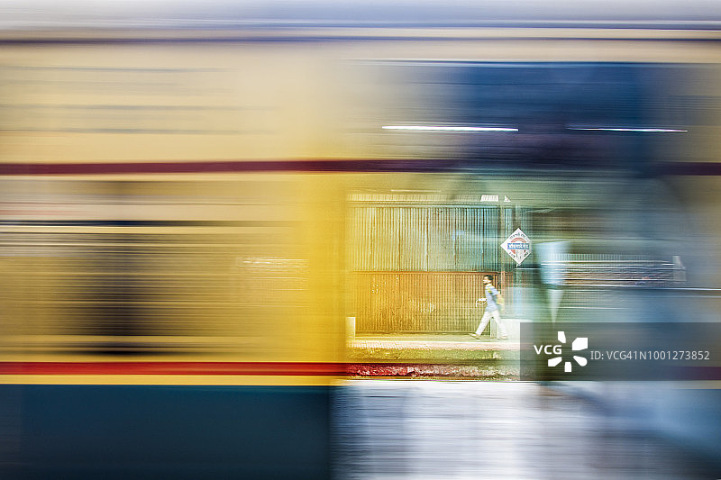 一名乘客走在当地火车站的站台上，另一列火车驶过图片素材