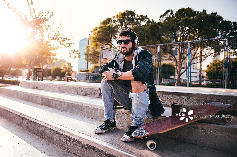年轻的滑板运动员在城市公园里听着音乐喝着咖啡放松图片素材