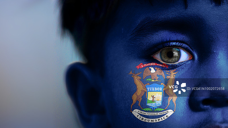 男孩的脸，看着镜头，裁剪的视图，脸上用数码技术放置了密歇根州州旗图片素材