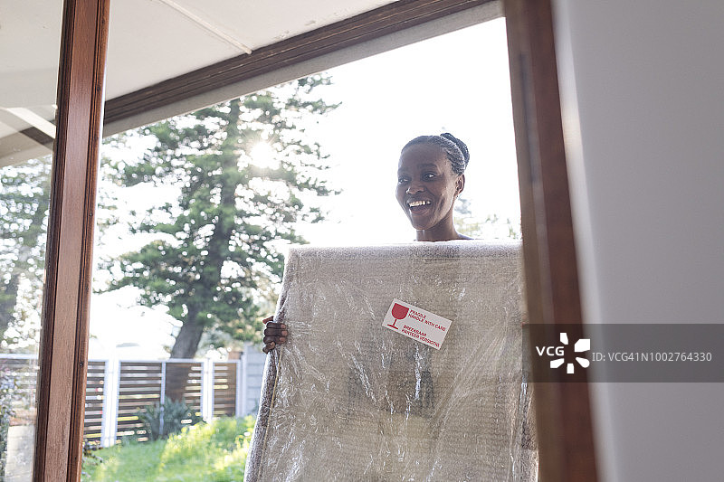 年轻女人抱着包裹好的画走进新家图片素材