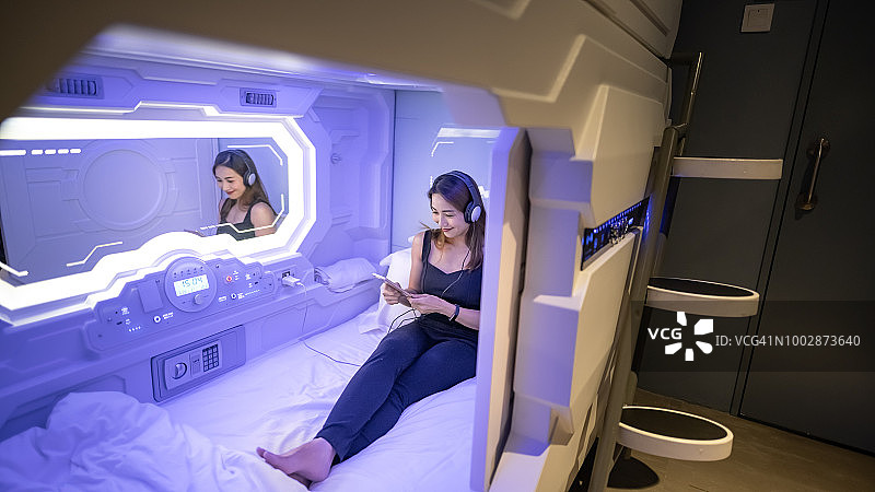 亚洲女性在胶囊酒店玩手机听音乐图片素材