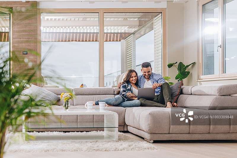 年轻情侣在客厅沙发上使用笔记本电脑图片素材