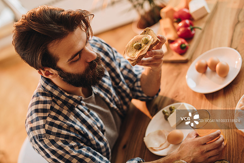 在餐桌旁吃三明治早餐的年轻男人图片素材