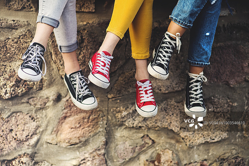 三个少女朋友穿着运动鞋在墙上盘腿而坐图片素材