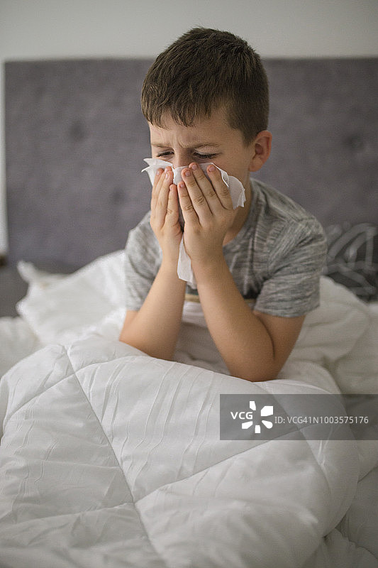 生病的小男孩在床上擦鼻涕图片素材
