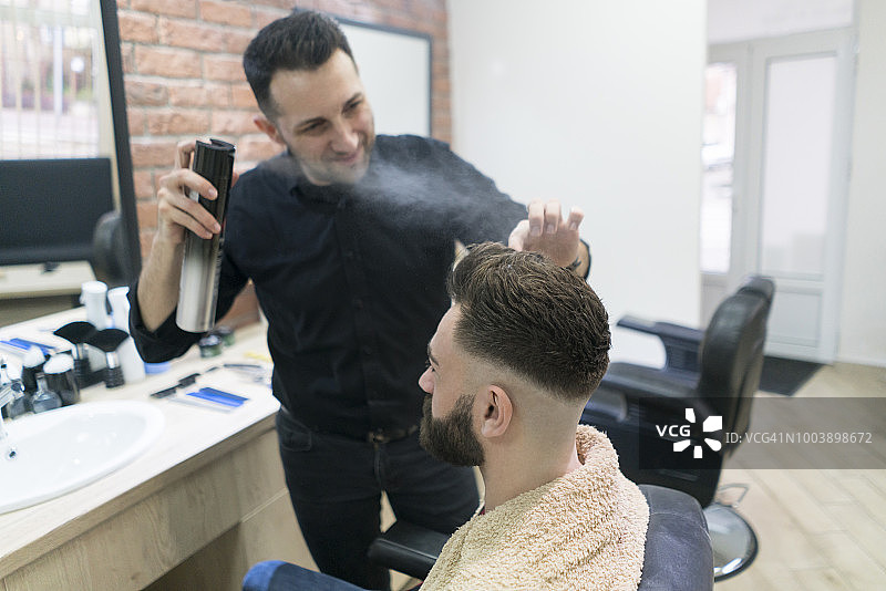 发型师在男人头发上喷发胶图片素材