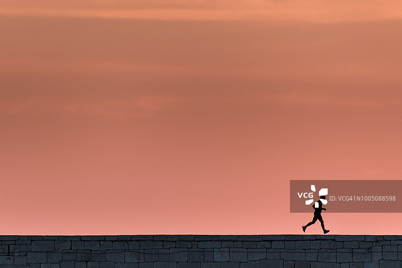夕阳下奔跑的男人剪影，美丽的粉橙色天空图片素材