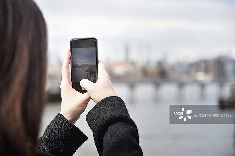 女人用手机拍摄东河对岸的景色图片素材