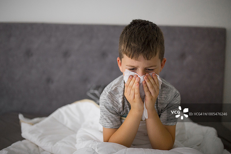 生病的小男孩在床上擦鼻涕图片素材