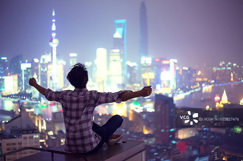 在城市屋顶上张开双臂的年轻男人图片素材