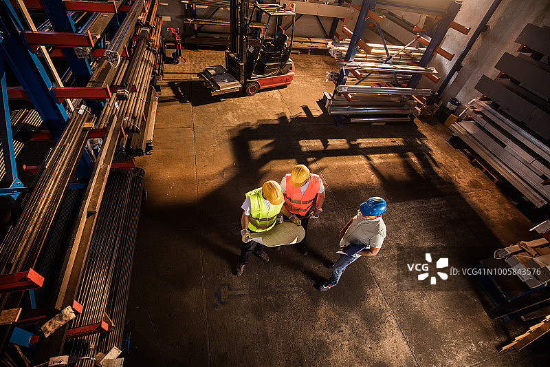 经理和两位工人在工业建筑中查看蓝图的俯视图图片素材