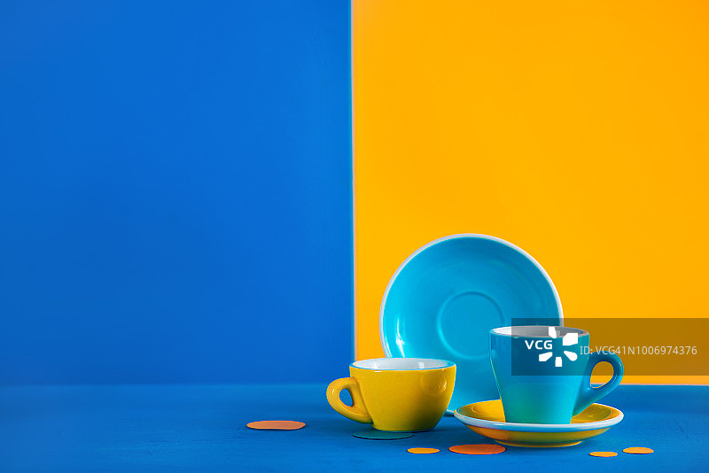鲜艳蓝黄色背景上的彩色咖啡杯图片素材