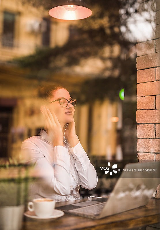 快乐的年轻女人坐在咖啡店里听音乐图片素材