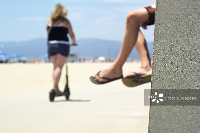 海滩自行车道上的踏板车骑手，前景是水泥墙图片素材