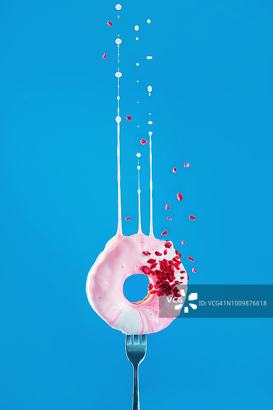 粉色甜甜圈，带有冻干覆盆子和充满活力的粉色釉料飞溅在鲜艳的蓝色背景上，带有复制空间的飞行食物概念图片素材
