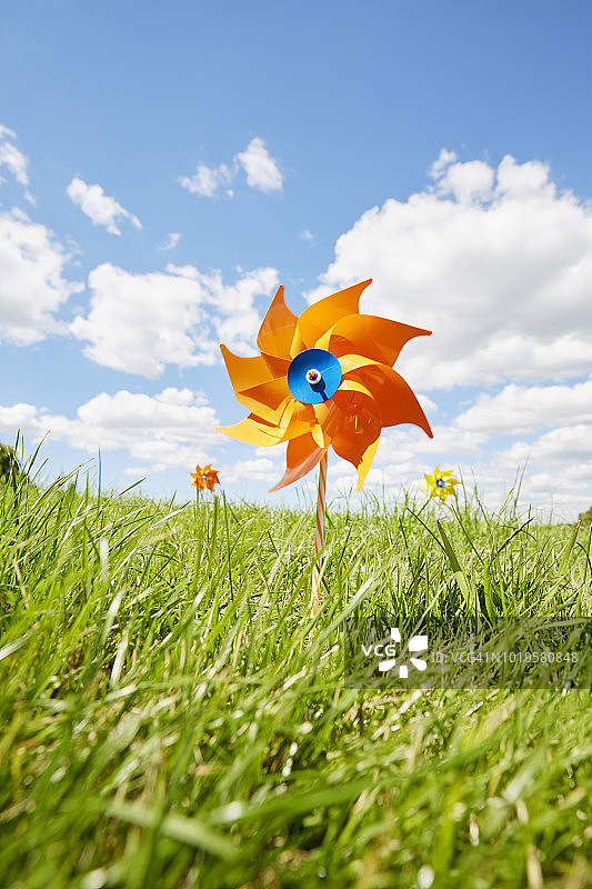 草地上对着天空的橙色风车图片素材