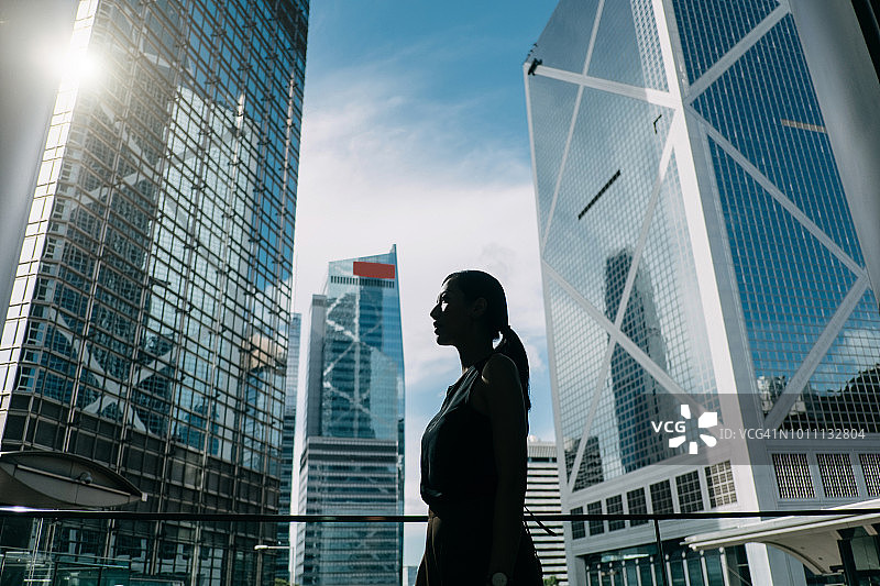 当代金融摩天大楼背景下，充满积极情绪的年轻女商人轮廓图片素材
