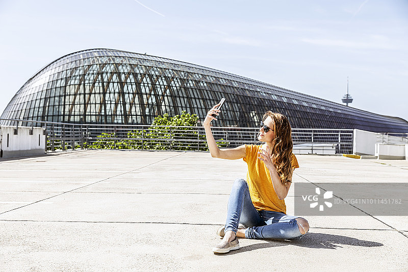 德国科隆：坐在停车场用智能手机自拍的微笑女士图片素材