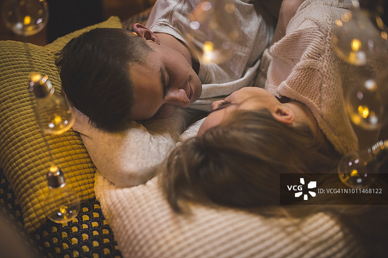 在床上拥抱，被童话灯光环绕的浪漫年轻情侣图片素材