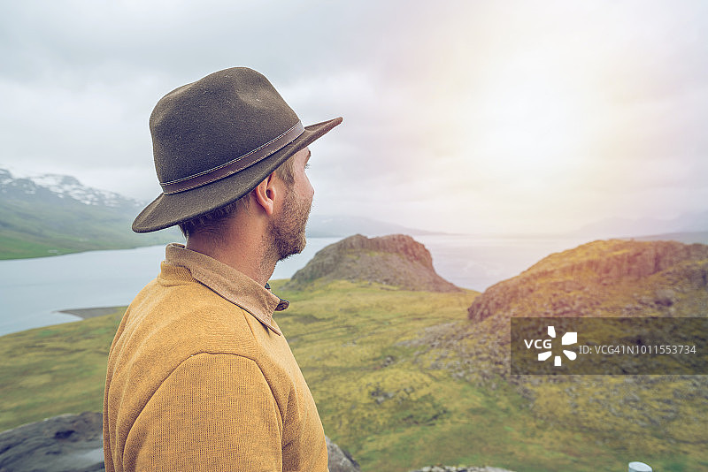 在冰岛峡湾顶端沉思的年轻男人图片素材