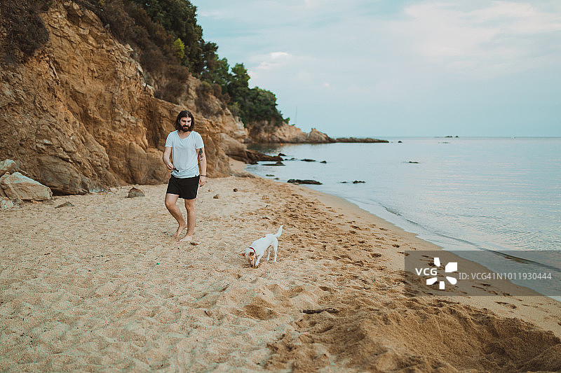 在希腊海滩与狗玩耍的嬉戏青年图片素材