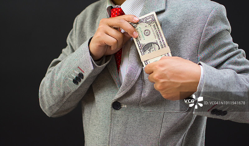 腐败概念：口袋里的钱，商人将钞票放入西装口袋图片素材