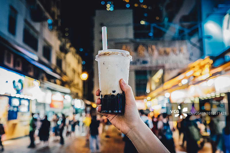 手持冰镇珍珠奶茶，背景是繁忙的城市街道夜景图片素材