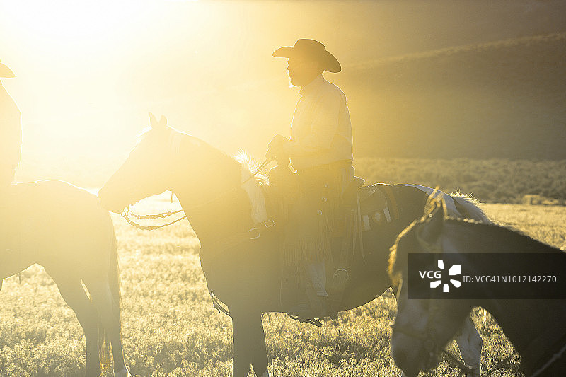 美国犹他州乡村山区日落时分骑马的背光成熟牛仔图片素材